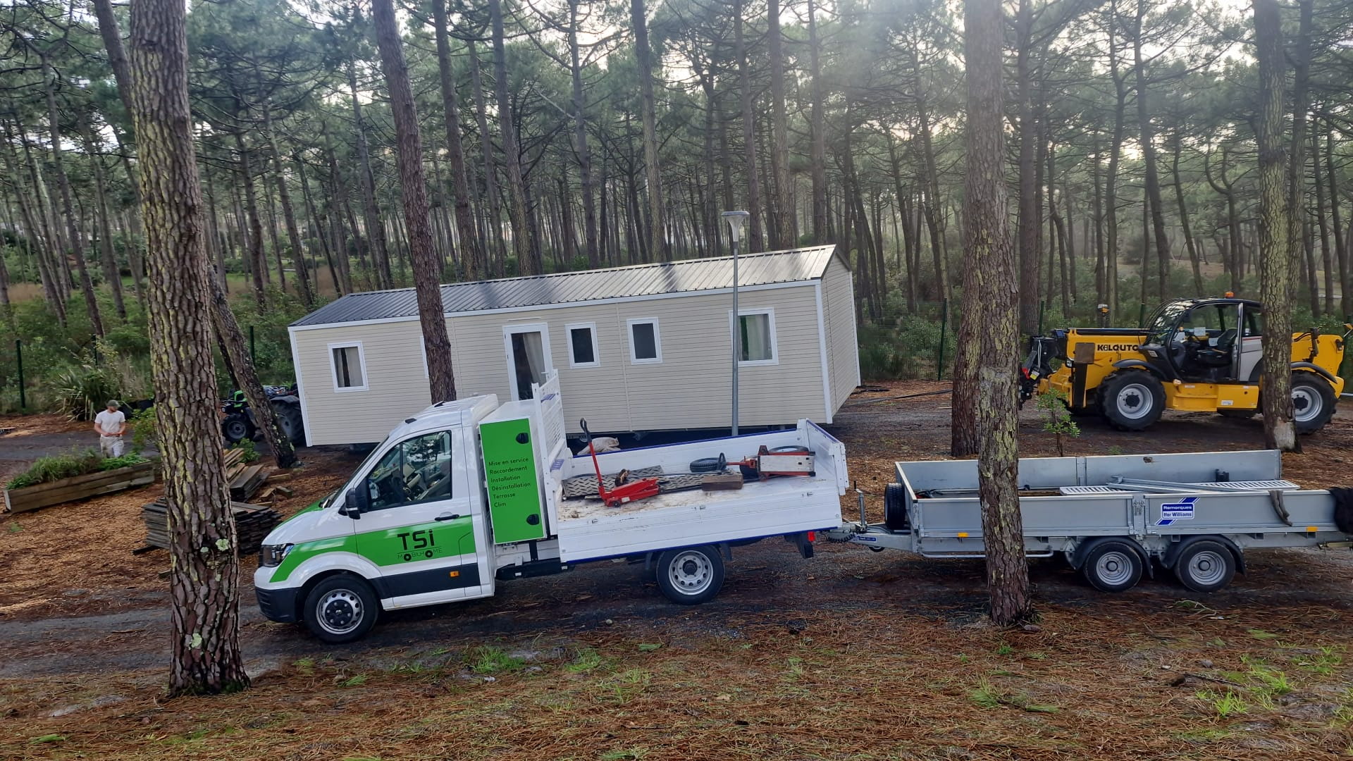 Convoi technique Zen Mobil-home : camion avec remorque et engin de levage pour l'installation d'un mobil-home neuf en zone boisée.